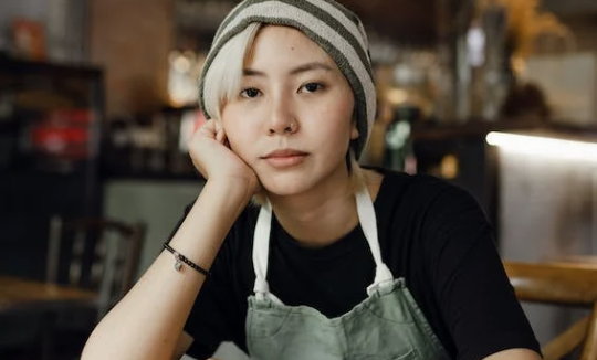 Asian Female Barista Not Happy with her job, sitting with her head resting on her hand/arm